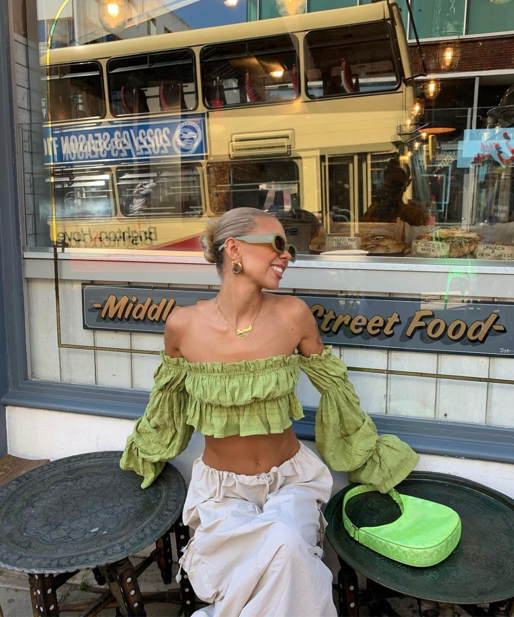 Daisy Birchall - blusa verde ciganinha, óculos e saia cargo bege - peças indispensáveis - Verão - sentada em um café - https://stealthelook.com.br