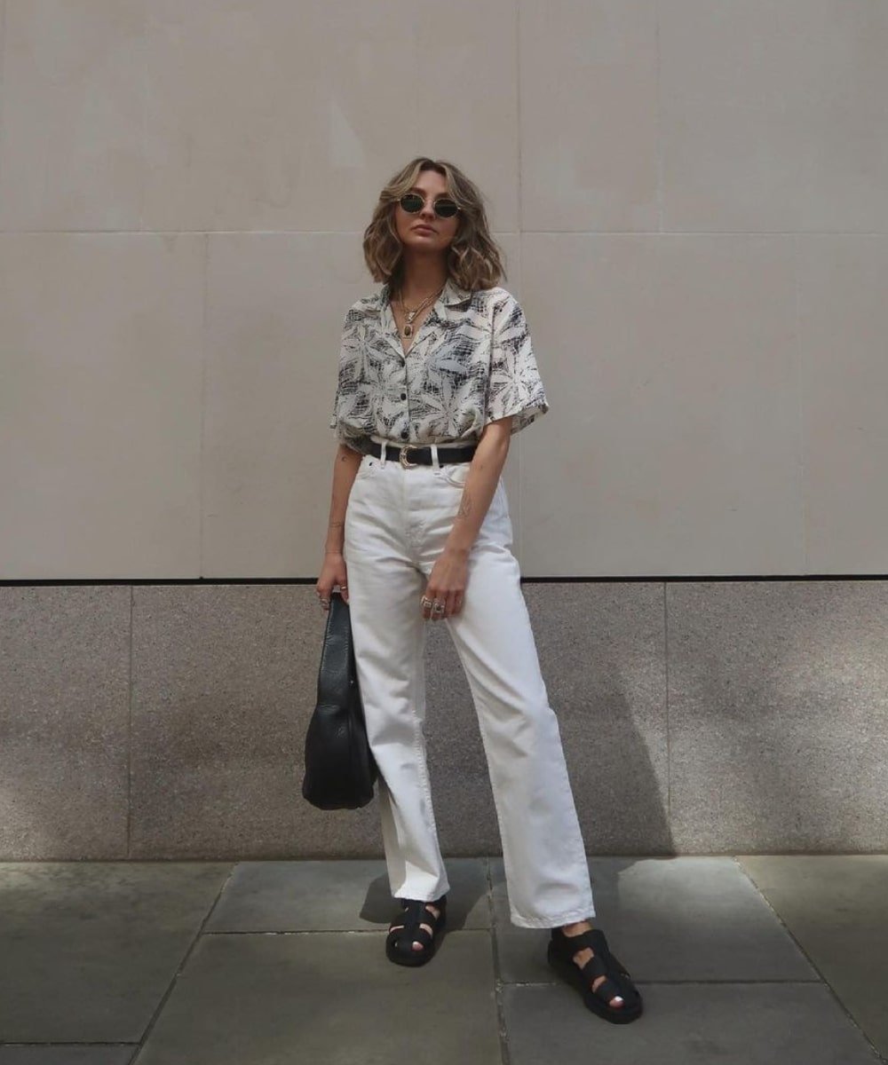 Chloe Hayward - calça jeans branca, camisa estampada e sandália fisherman preta - looks de verão - Verão - andando na rua usando óculos de sol - https://stealthelook.com.br