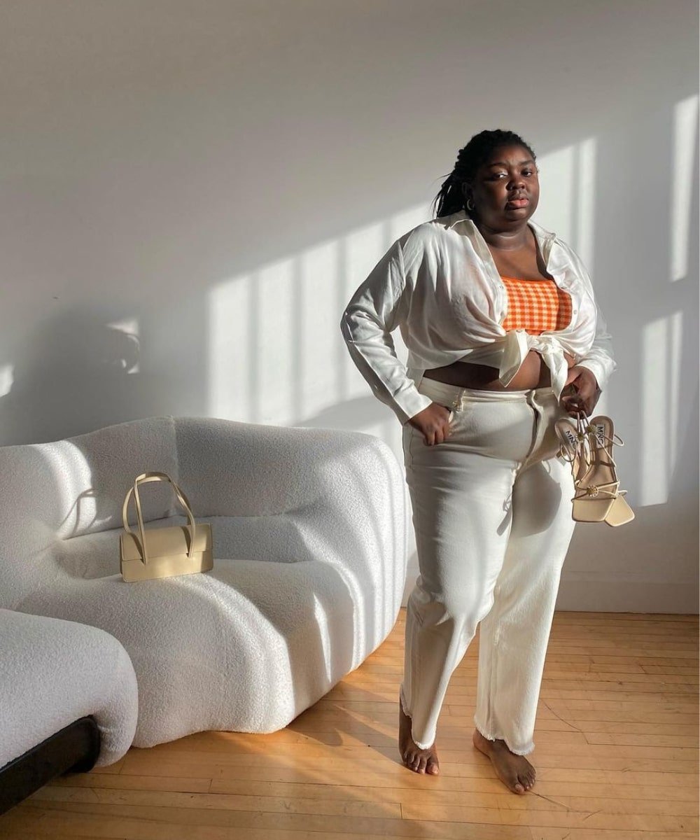 Abisola Omole - calça branca, cropped, camisa branca - looks de verão - Verão - em pé em uma sala e segurando uma sandália na mão - https://stealthelook.com.br