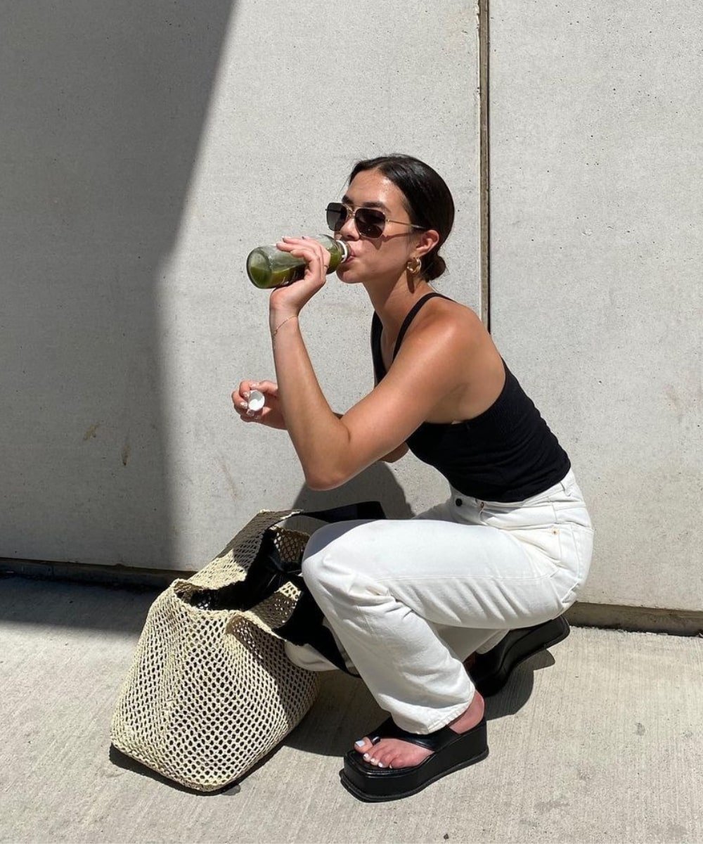 Sasha Mei - calça branca, top preto e tamanco de plataforma - looks de verão - Verão - agachada na rua tomando suco - https://stealthelook.com.br