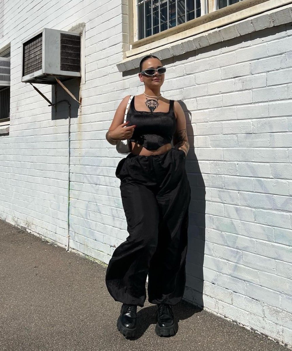 Chelsea Butcher - calça preta estilo parachute pants, corset preto e tenis preto - calças da moda 2023 - Primavera - em pé na rua usando óculos de sol - https://stealthelook.com.br