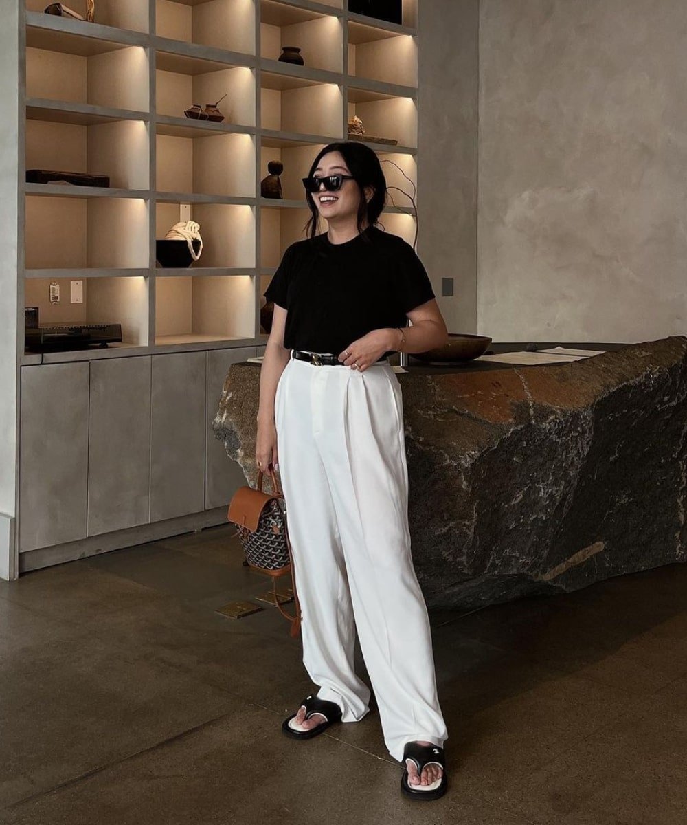 Alyssa Lenore - calça drapeada branca, blusa preta e chinelos - tendência de moda - Verão - em pé na rua usando óculos de sol - https://stealthelook.com.br