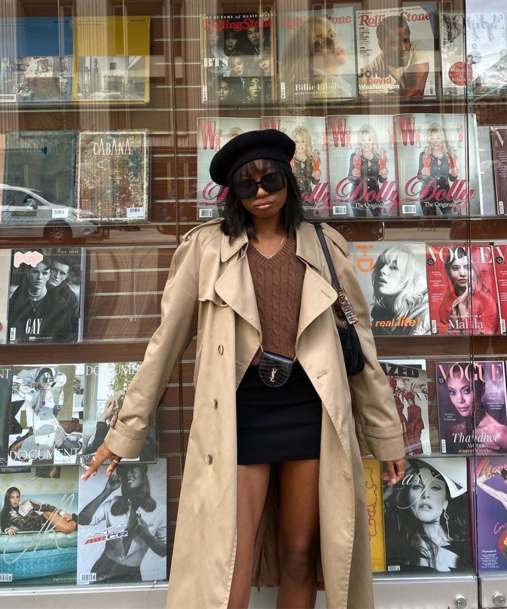 Chanel McKinsie - minissaia preta, cropped marrom e trench coat bege - tendências de moda - Outono - em pé na rua usando óculos de sol e uma boina - https://stealthelook.com.br