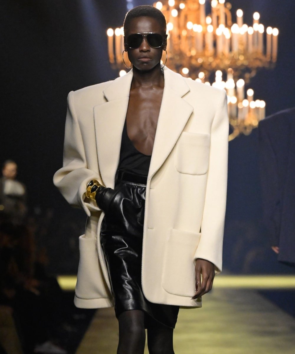 Desfile F/W 2023 Saint Laurent - blazer off white super estruturado, saia de couro, óculos escuros e acessórios dourados - anos 80 - inverno - modelo andando na passarela - https://stealthelook.com.br