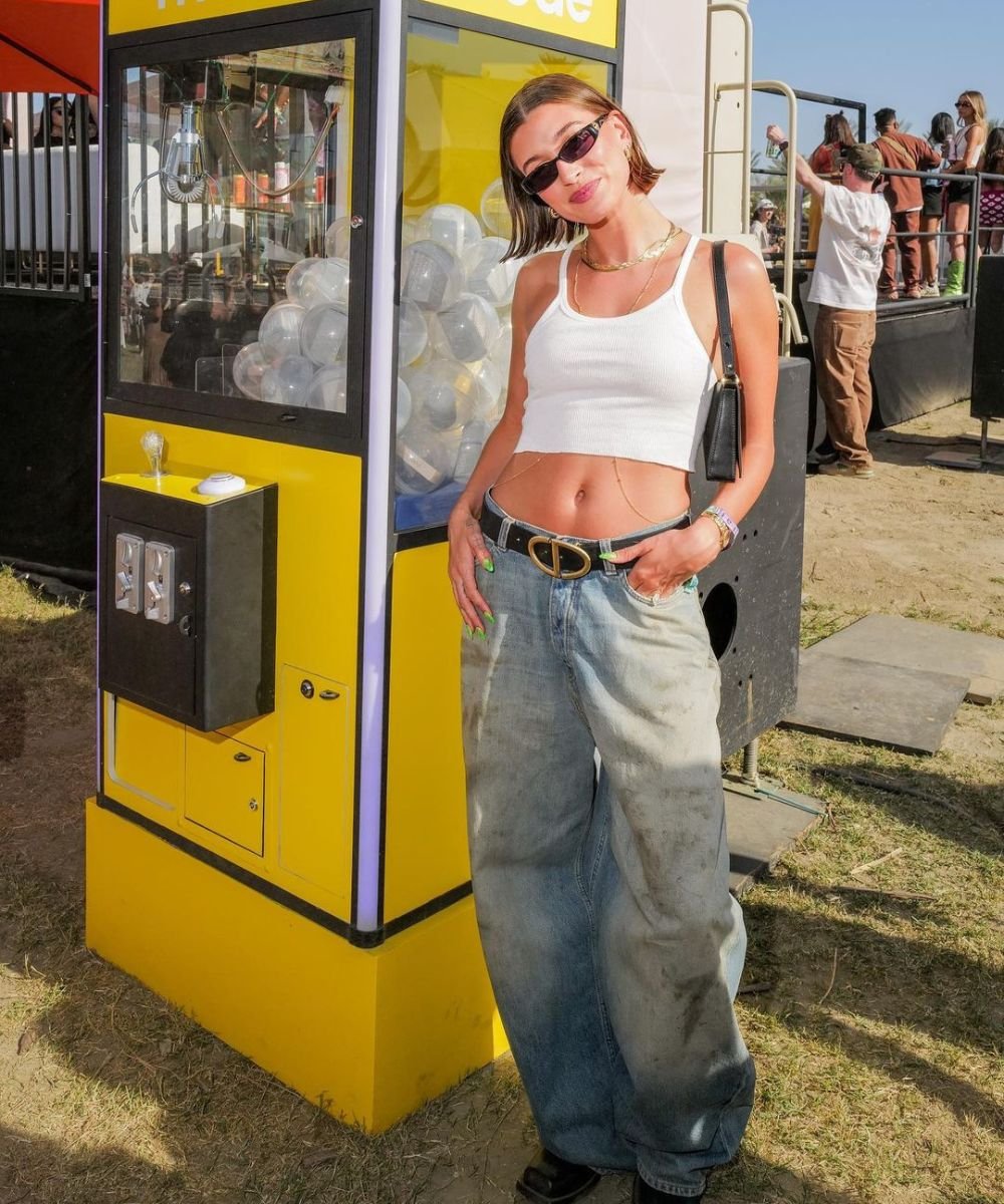 Hailey Bieber - calça jeans baggy, regata branca e óculos escuros - looks do Coachella - verão - em pé encostada em uma parede cinza - https://stealthelook.com.br