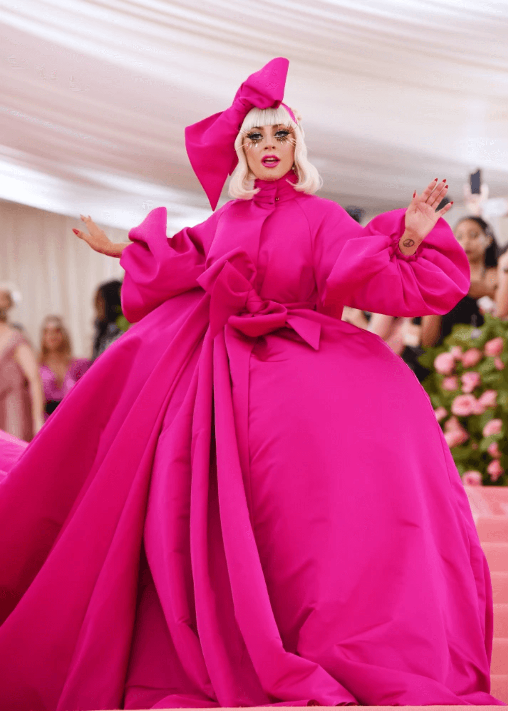 Lady Gaga - vestido rosa bufante - Met Gala - primavera - em pé com os dois braços abertos e com cara de assutada - https://stealthelook.com.br