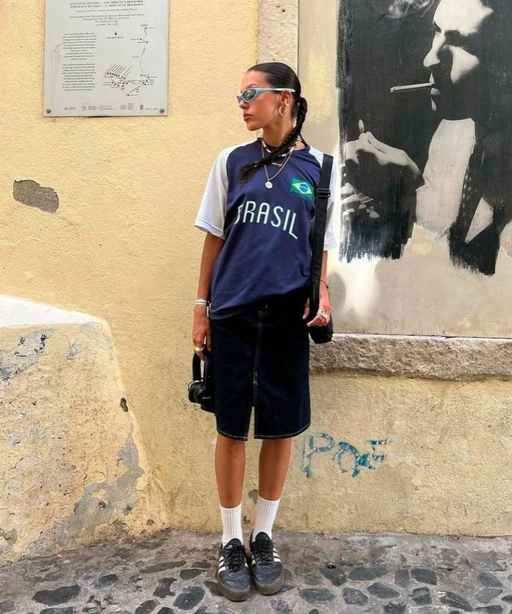 Maina Suarez - bermuda preta, camisa de time azul, meias brancas e tenis preto - tendências do TikTok - verão - em pé na rua usando óculos de sol - https://stealthelook.com.br