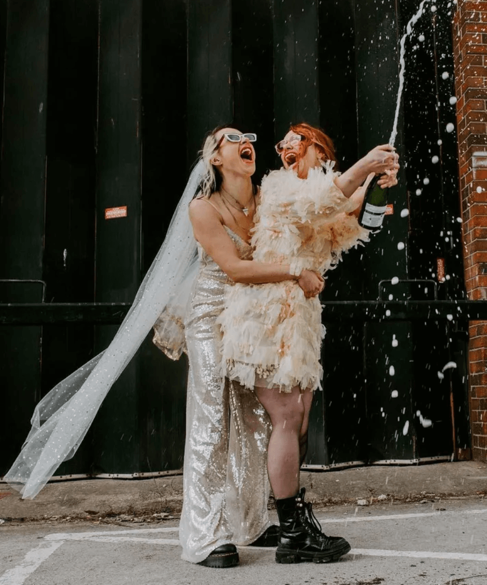 Casamento anti-bride - casal usando vestidos de festa e óculos de sol - anti-bride - verão - casal abraçado e comemorando com buque na mão - https://stealthelook.com.br