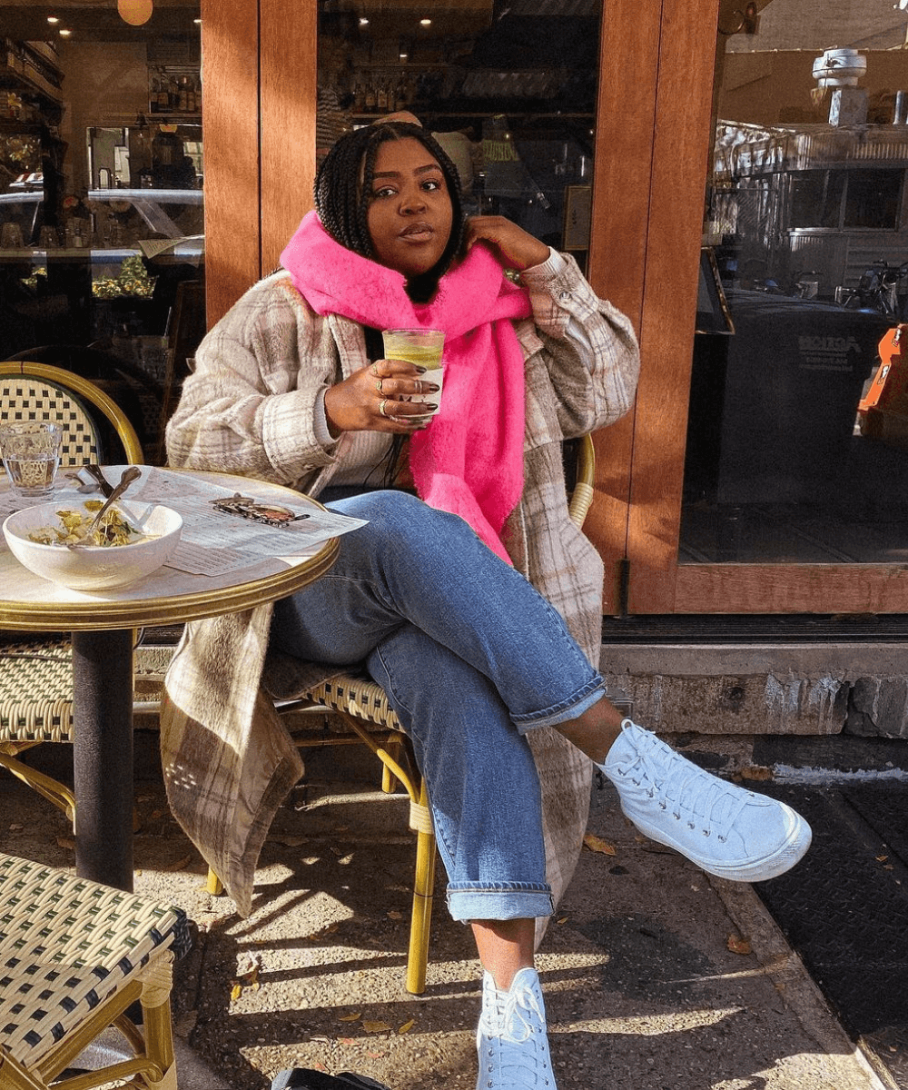 Candace Molatore - calça jeans, shacket xadrez, cachecol rosa e tênis branco - looks com xadrez - inverno - sentada em um café na rua - https://stealthelook.com.br