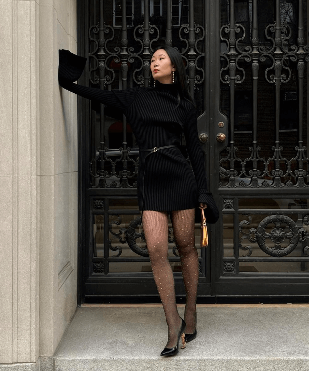 Caroline Lin - vestido preto de manga longa, meia-calça com brilhos e scarpin preto - looks de festa - inverno - em pé na rua em cima de uma escada - https://stealthelook.com.br