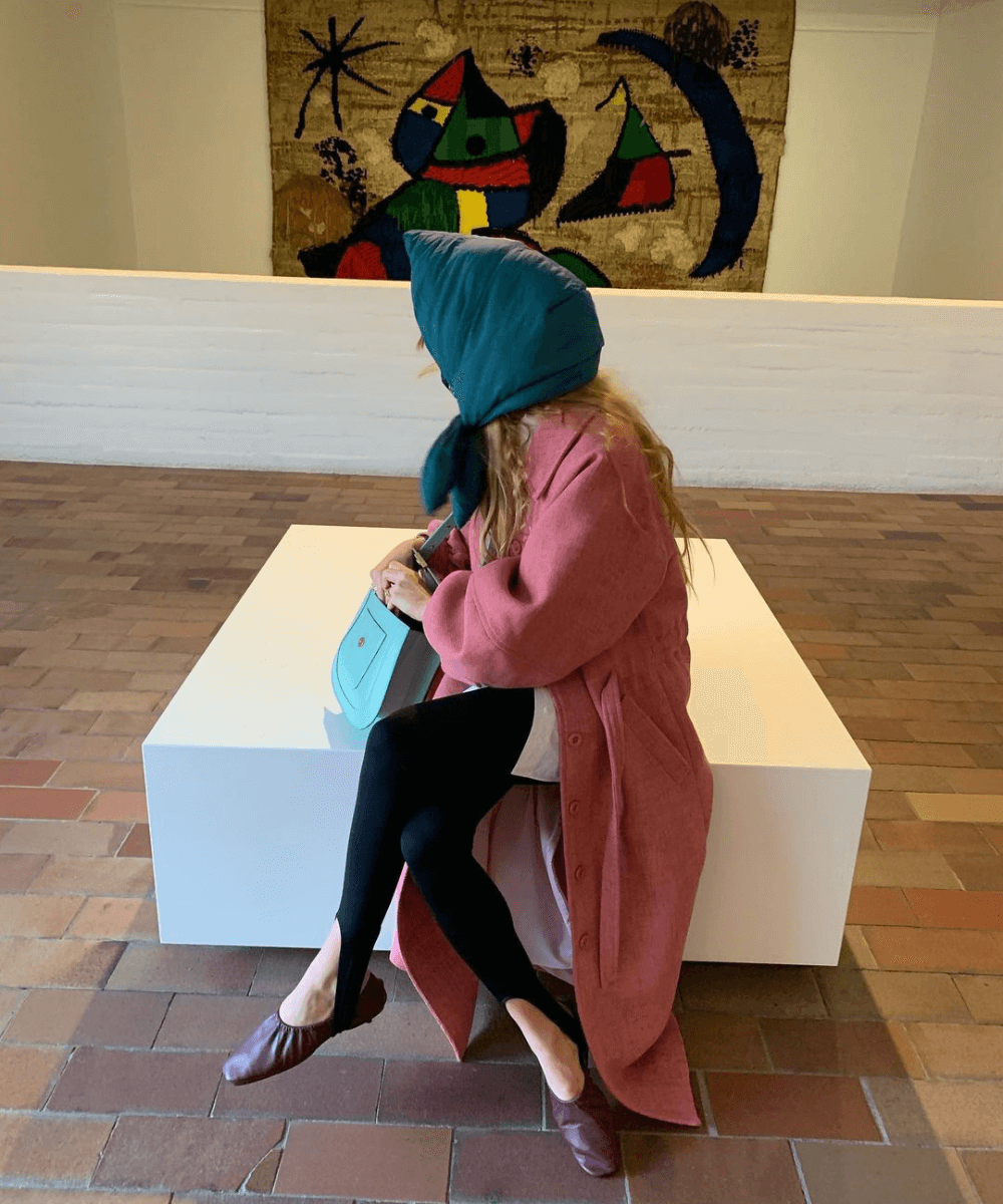 Blanca Miró Scrimieri - calça legging com pezinho, sapatilhas vermelhas e casaco longo rosa - Stirrup Pants - outono - mulher sentada em um banco olhando para o lado e com um lenço na cabeça - https://stealthelook.com.br