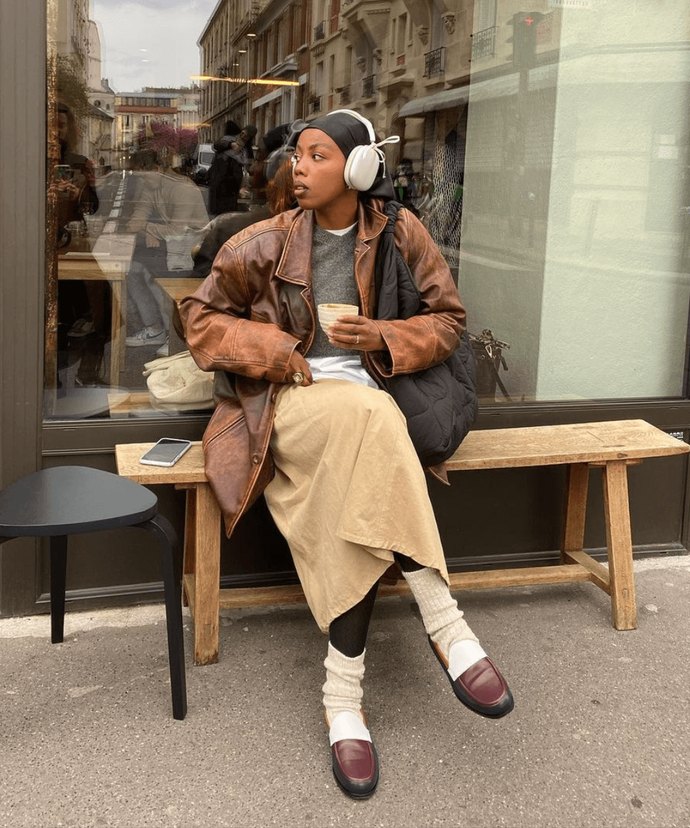 @blackmaroccan - saia midi bege, meia-calça preta, polaina e tênis adidas samba - acessório tendência - inverno - mulher negra sentada em um banco na rua olhando para o lado - https://stealthelook.com.br