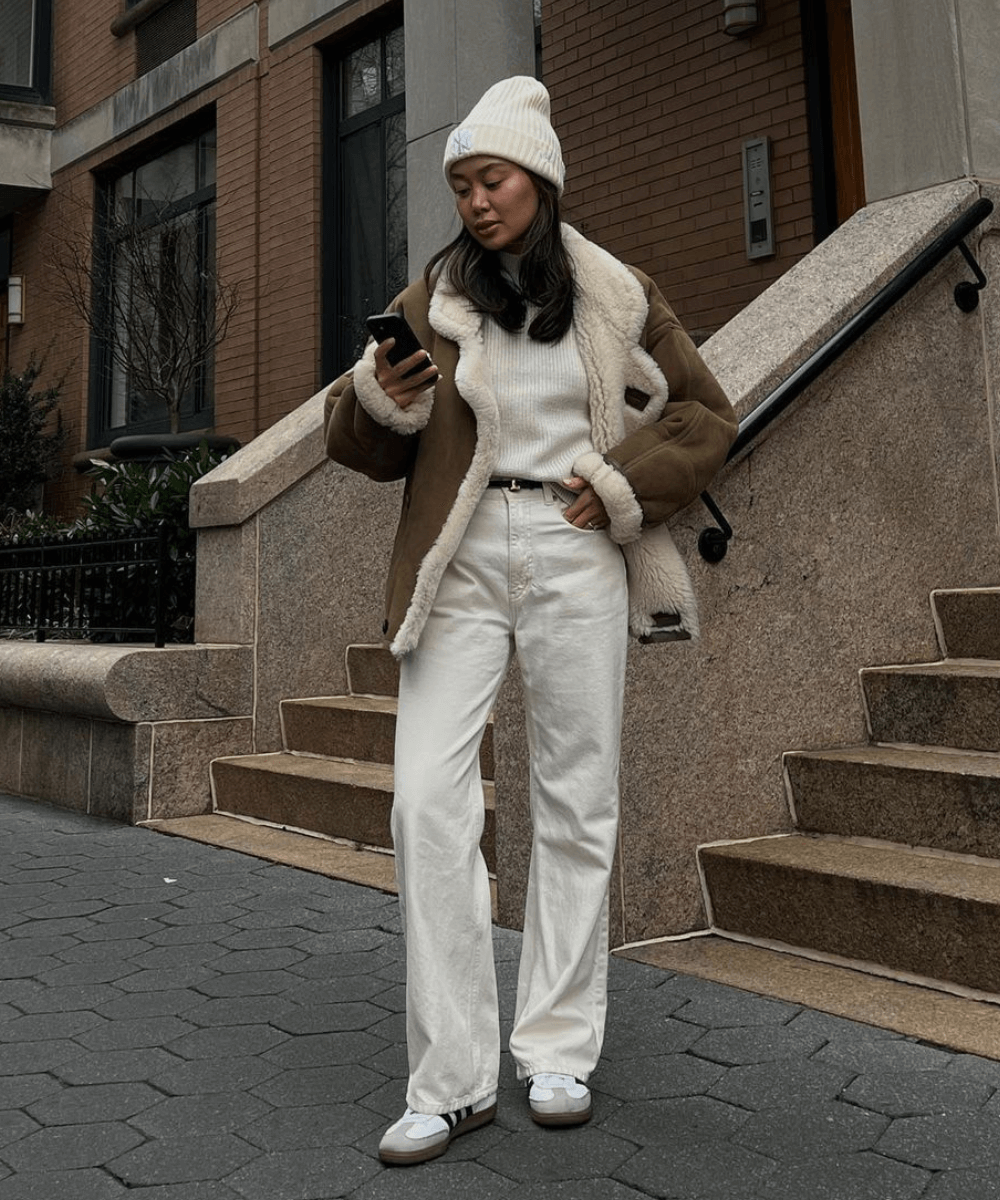 Linh Niller - calça branca, tênis adidas samba, trico branco, jaqueta de couro marrom e gorro branco - looks de inverno - inverno - mulher em pé na rua - https://stealthelook.com.br