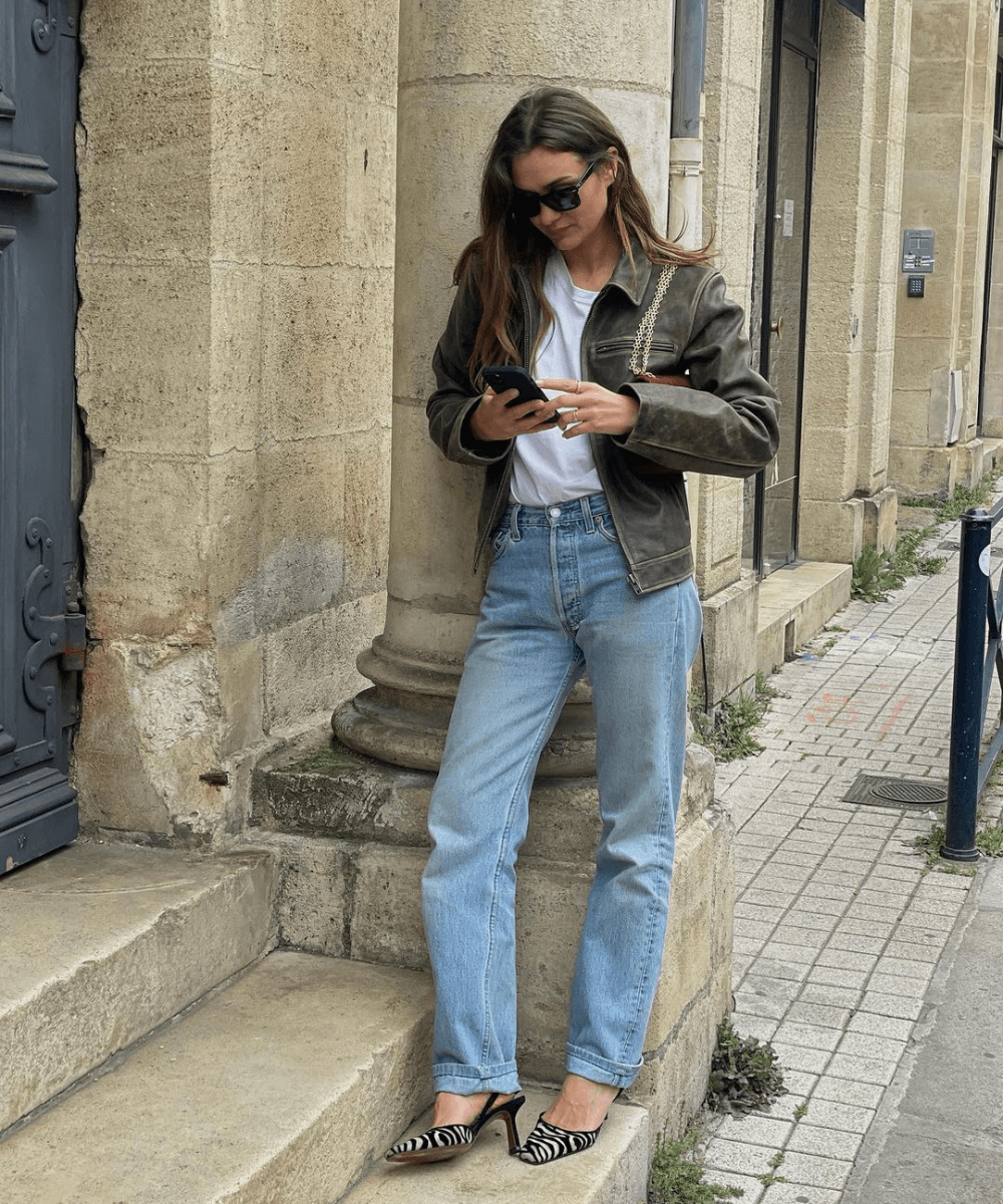 Adenorah | @annelauremais - calça jeans, regata branca, jaqueta de couro estonada - inverno 2023 - inverno - mulher em pé na rua usando óculos de sol e usando o celular - https://stealthelook.com.br