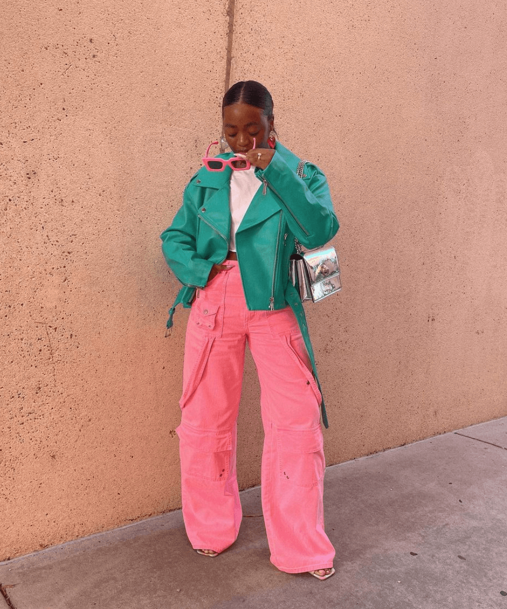 @thenxcstyle - calça cargo rosa, jaqueta de couro verde e óculos rosa - inverno 2023 - inverno - mulher em pé na rua tirando o óculos de sol - https://stealthelook.com.br