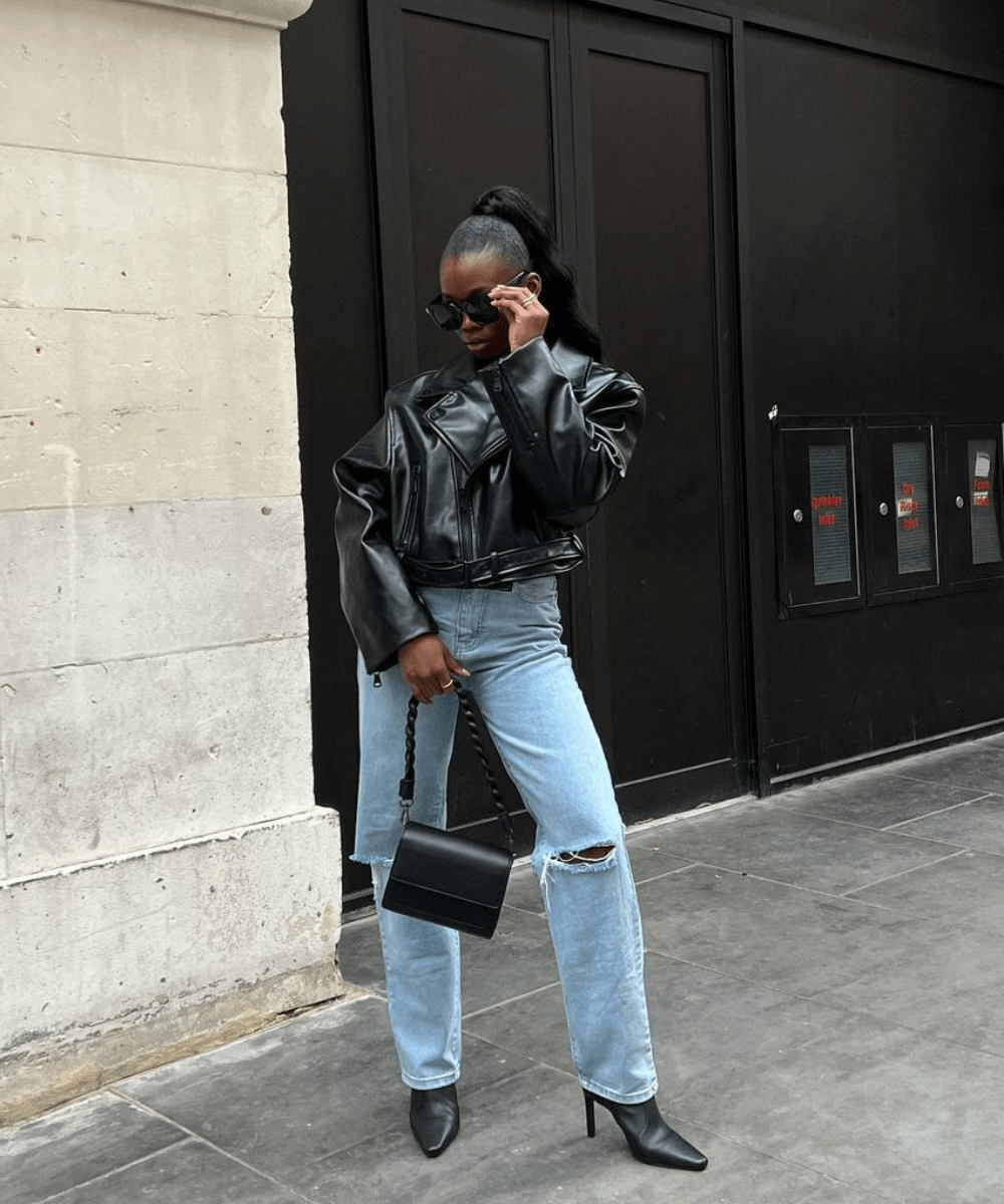 Rabia Cissokho - calça jeans, bota preta de bico fino e jaqueta de couro preta - inverno 2023 - inverno - em pé na rua usando óculos de sol - https://stealthelook.com.br