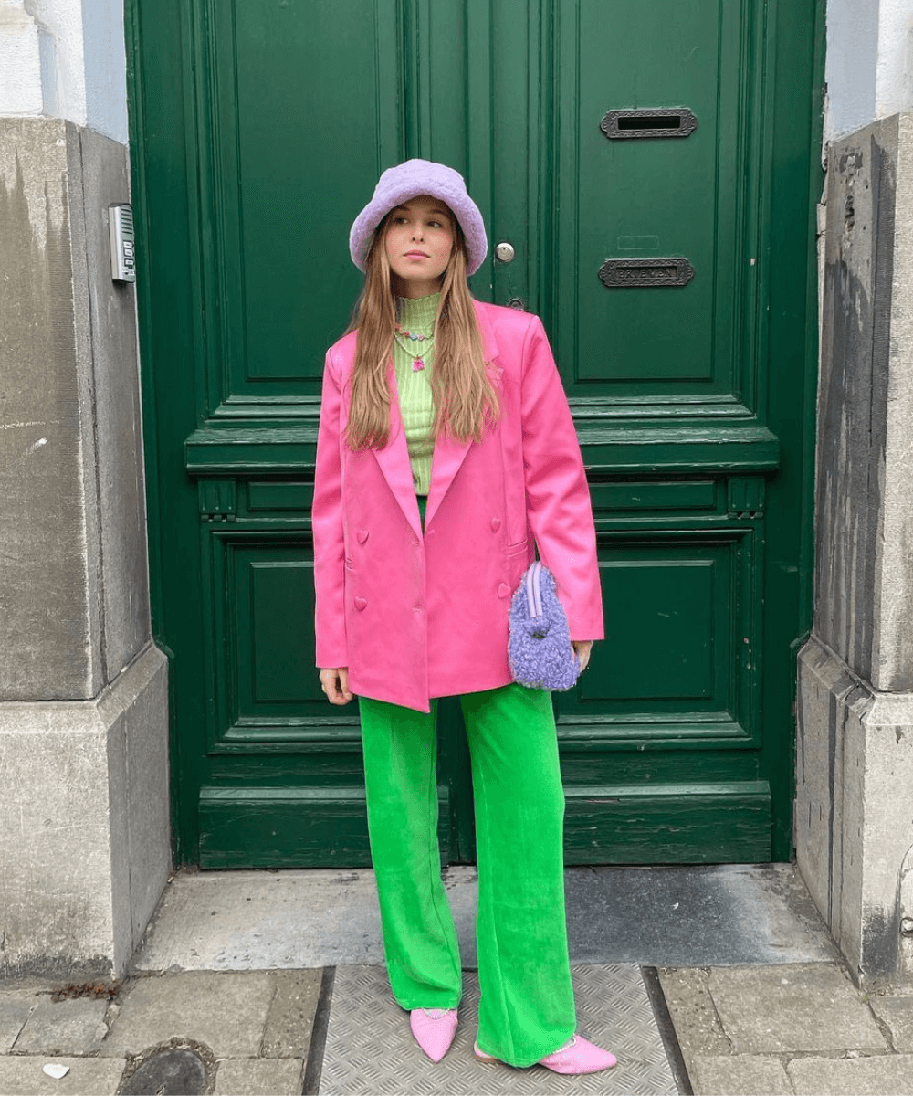 Anaïs Van Oekel - calça verde, blazer rosa, scarpin rosa e bucket hat lilás - looks de inverno - inverno - mulher loira em pé na rua usando um bucket hat de pelúcia - https://stealthelook.com.br