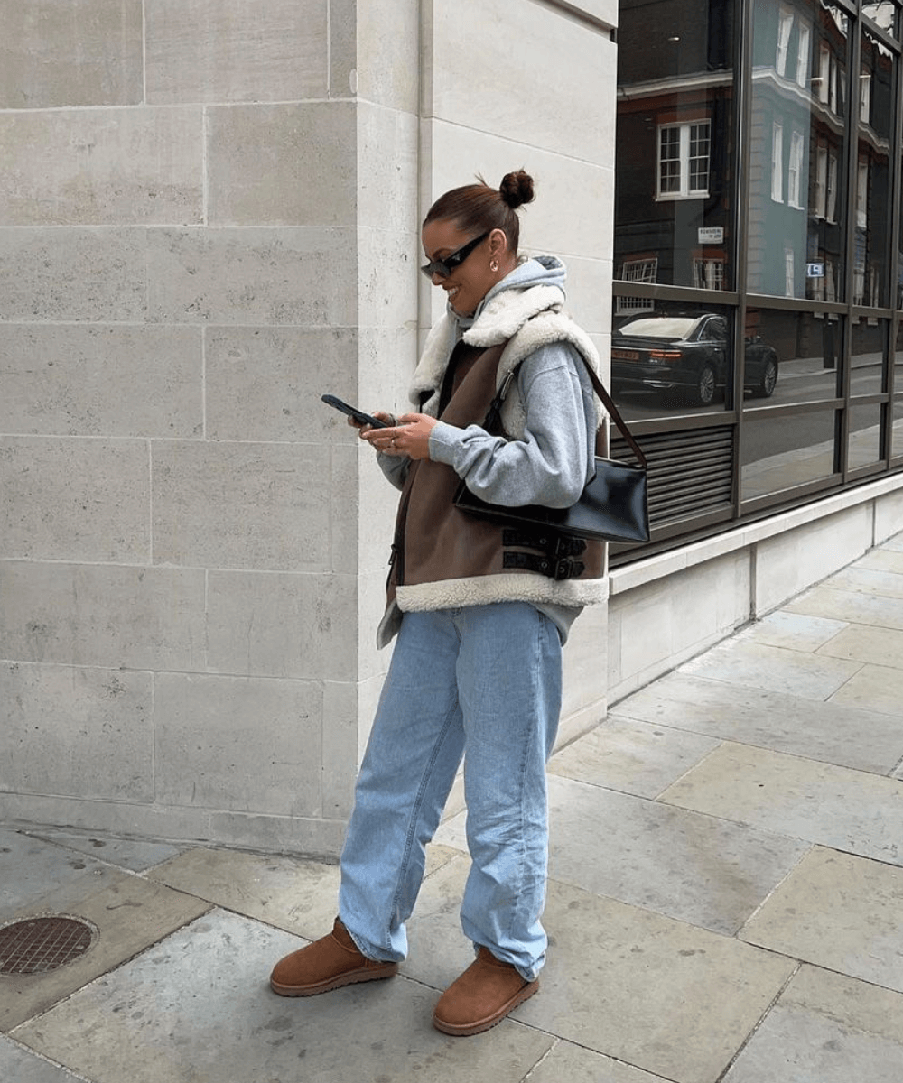Jamie Firth - calça jeans wide, bota ugg, moletom cinza e colete shearling - bota tendência - inverno - mulher em pé de lado na rua - https://stealthelook.com.br