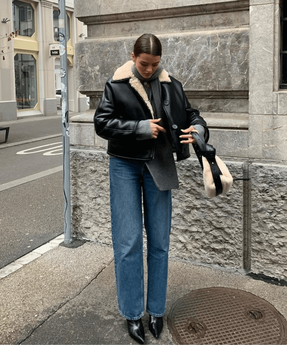 @maryljean - calça jeans, bota preto de bico fino e jaqueta aviador preta - looks de inverno - inverno - mulher em pé na rua segurando uma bolsa - https://stealthelook.com.br
