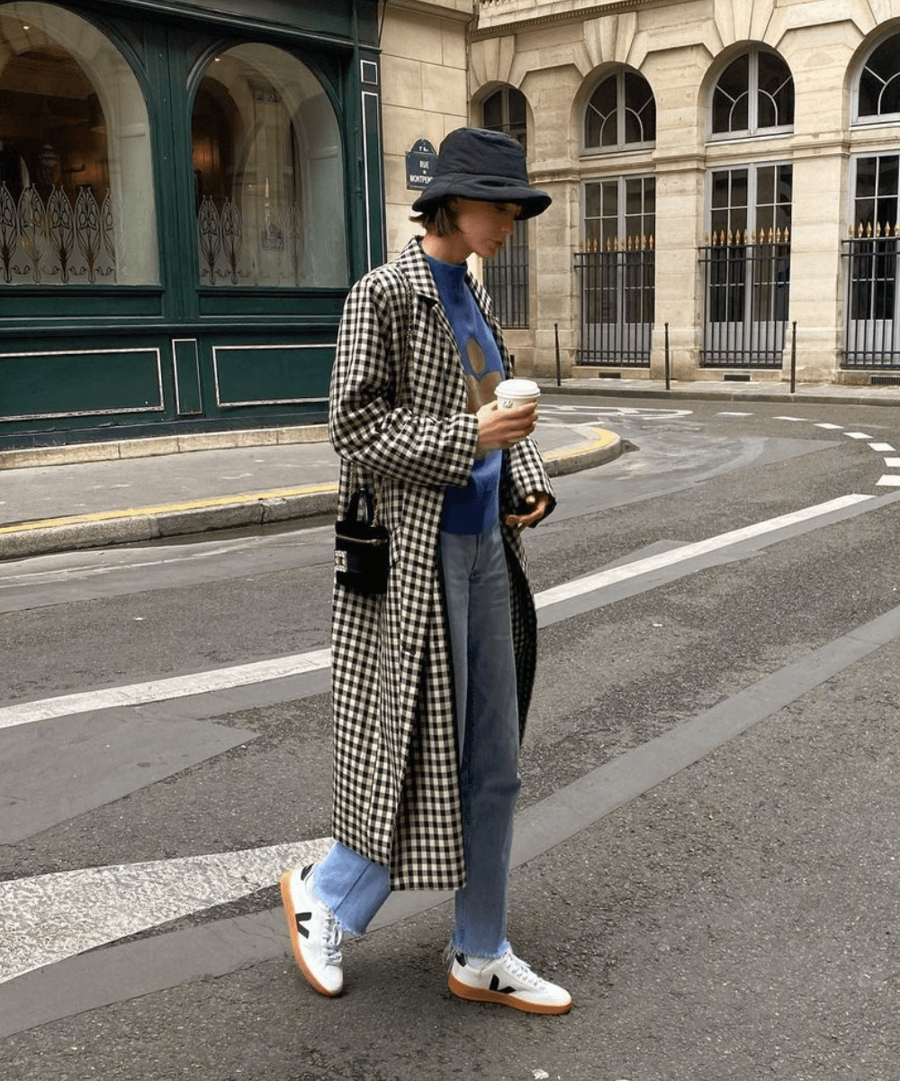 Marie Gilliot - calça jeans, tênis vert, tricô azul e casaco longo xadrez - tênis tendência - inverno - mulher andando na rua usando bucket hat - https://stealthelook.com.br
