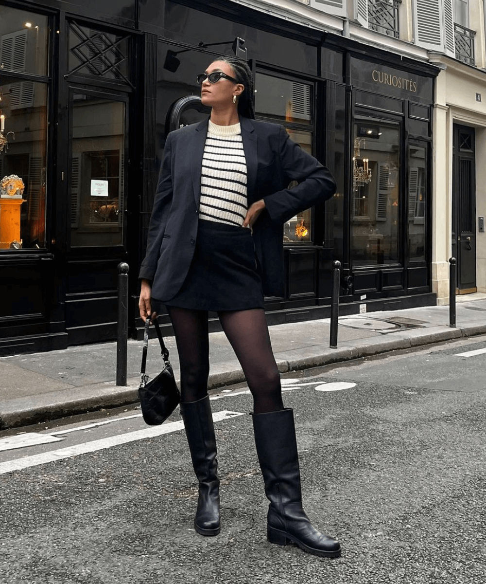 @lenafarl - minissaia preta, tricô listrado, bota de cano longo e tricô listrado - inverno 2023 - inverno - mulher em pé na rua usando óculos de sol - https://stealthelook.com.br