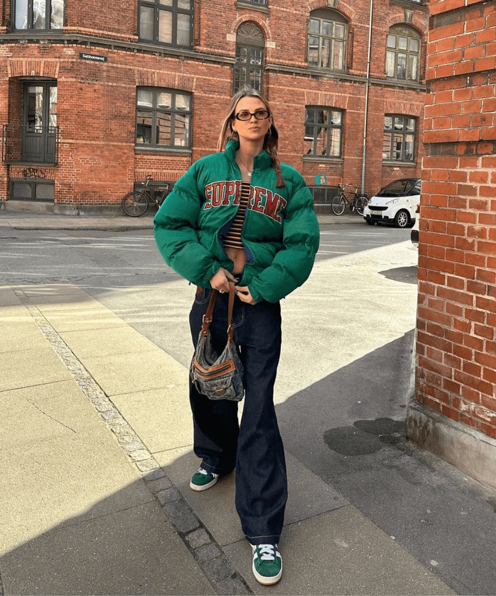 Anna Winck - calça jeans, tênis adidas verde, blusa listrada e jaqueta puffer verde - looks com jaqueta puffer - inverno - mulher loira sorrindo e andando na rua - https://stealthelook.com.br