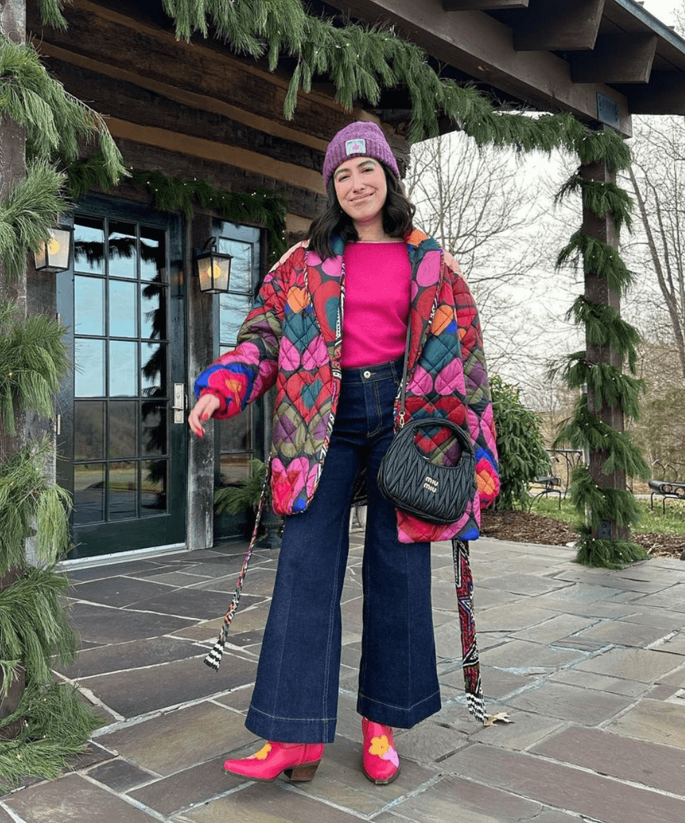 @aprillockhart - calça jeans, bota rosa e jaqueta puffer estampada de coração - looks com jaqueta puffer - inverno - mulher de gorro roxo em pé na rua - https://stealthelook.com.br