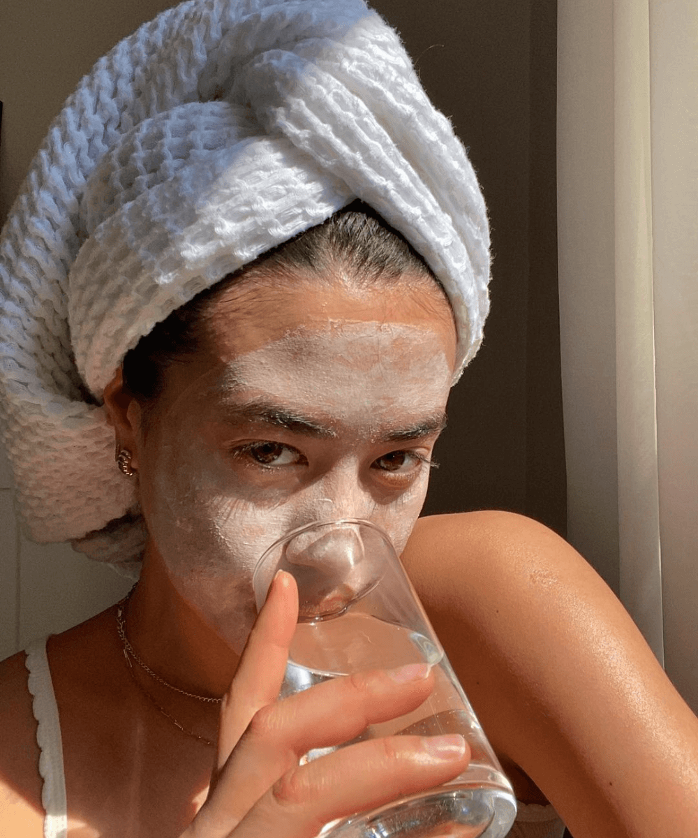 Sasha Mei -     - dermatite atópica - verão - mulher com toalha na cabeça, máscara facial branca e bebendo água - https://stealthelook.com.br
