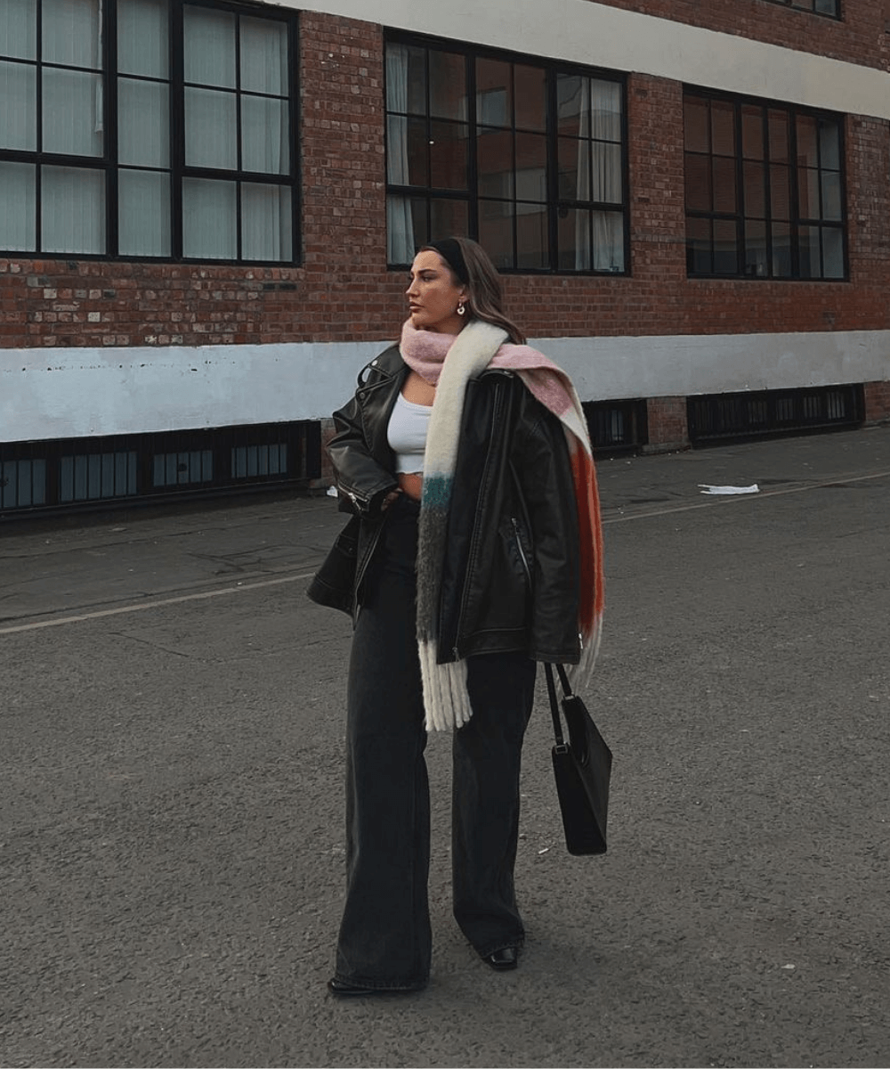 Faye Queenan - calça preta, cropped branco, jaqueta de couro preta e cachecol longo colorido - jaqueta biker - inverno - mulher loira andando na rua - https://stealthelook.com.br