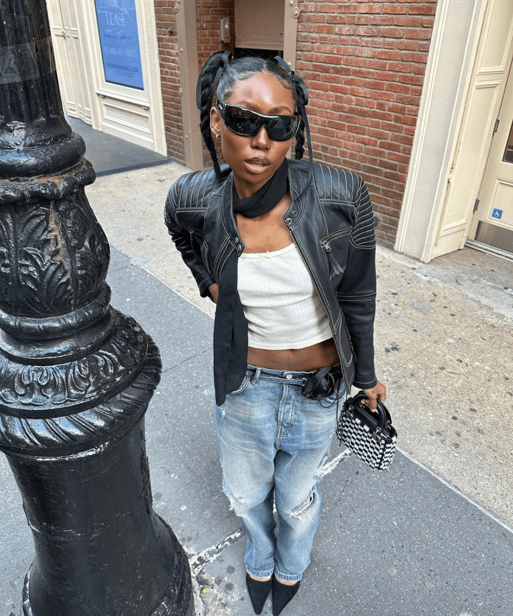 Chanel Mckinsie - calça jeans, cropped branco, óculos escuros e jaqueta de couro preta - jaqueta biker - outono - mulher negra em pé na rua usando óculos de sol - https://stealthelook.com.br