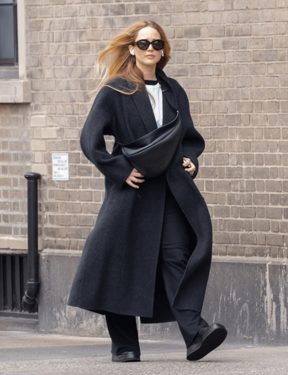 Jennifer Lawrence - calça preta, sobretudo longo preto, óculos de sol e tênis preto - Jennifer Lawrence - inverno - mulher loira andando na rua usando óculos de sol - https://stealthelook.com.br