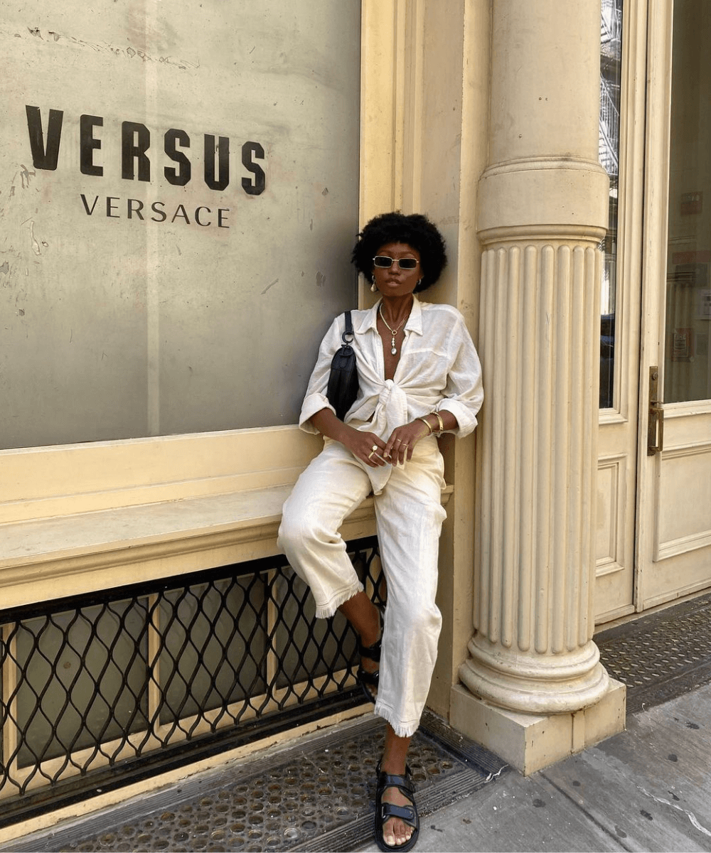 Chanel Mckinsie - calça off white, camisa branca, papete e óculos de sol - calça bege - verão - mulher negra andando na rua usando óculos de sol - https://stealthelook.com.br