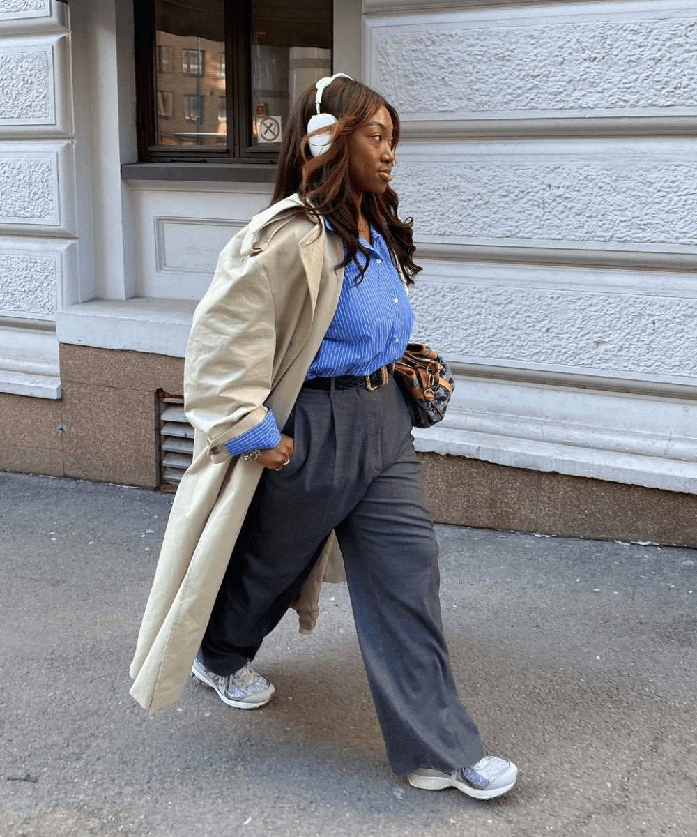 Nnenna Echem - calça de alfaiataria, camisa azul, casaco bege e tênis - tênis esportivos - inverno - mulher negra andando na rua de fone - https://stealthelook.com.br