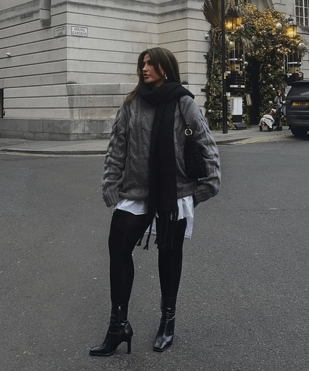 Faye Queenan - tricot cinza, legging preta, bota de salto e camisa branca por baixo - looks com tricô - inverno - mulher em pé na rua - https://stealthelook.com.br