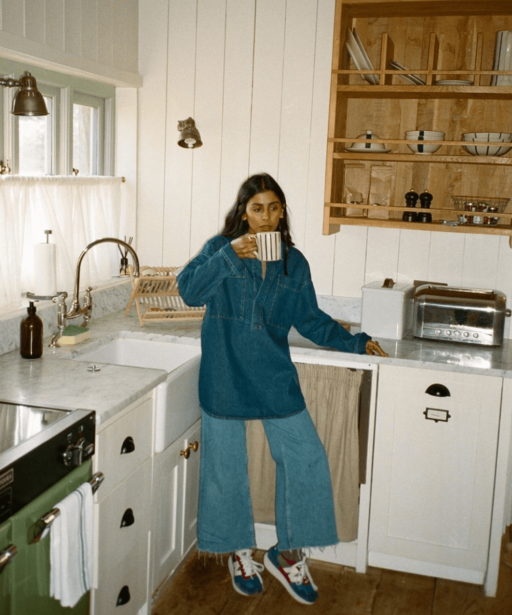 @monikh - calça jeans, camisa jeans e tênis - itens de cozinha - outono - mulher em pé na cozinha bebendo em uma xícara - https://stealthelook.com.br