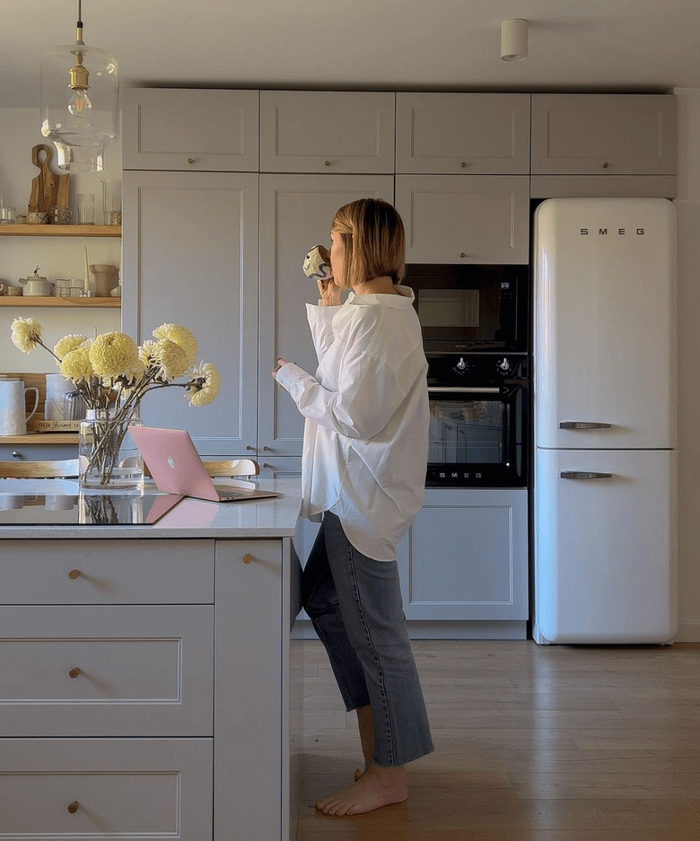 @domsli22 - calça jeans e camisa branca oversized - itens de cozinha - inverno - mulher em pé em uma cozinha bebendo café - https://stealthelook.com.br
