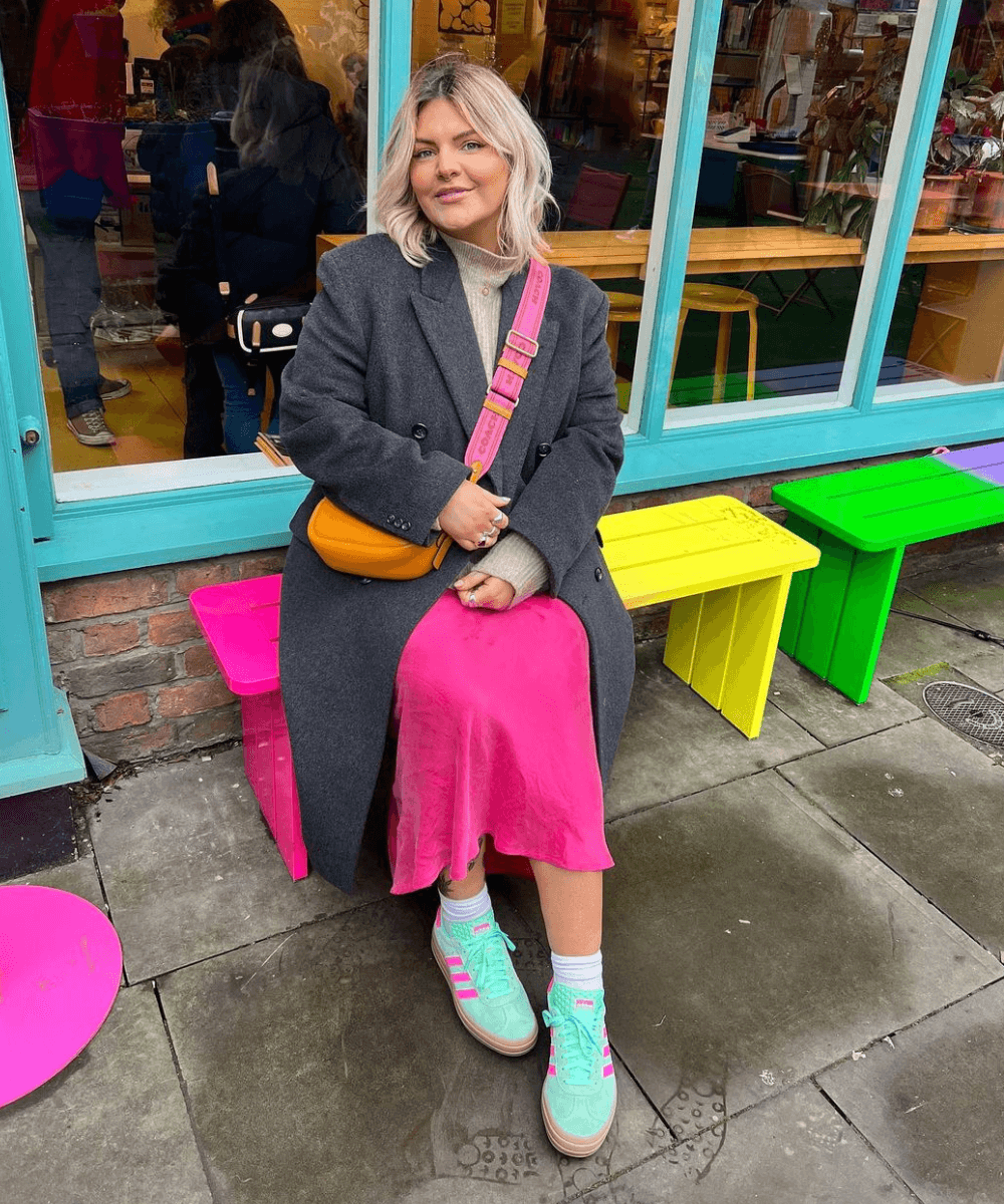 Libby Faulkner - vestido rosa, tricot e sobretudo cinza, com tênis rosa - inverno 2023 - inverno - mulher loira sentada em um banco na rua - https://stealthelook.com.br