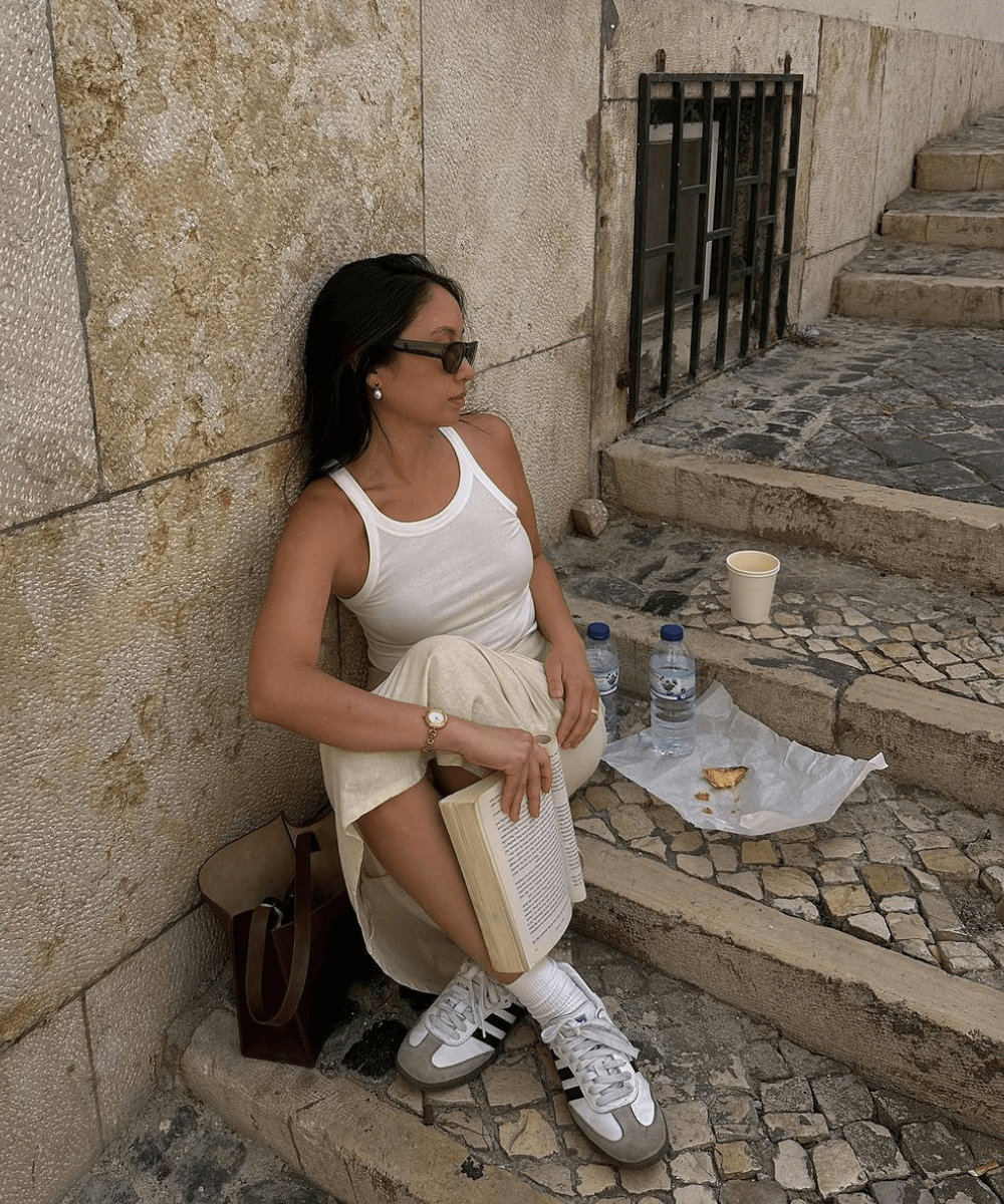 Jordan Santos - saia midi bege, regata branca e tênis adidas samba - looks fáceis - verão - mulher de óculos sentada no chão em uma escada - https://stealthelook.com.br