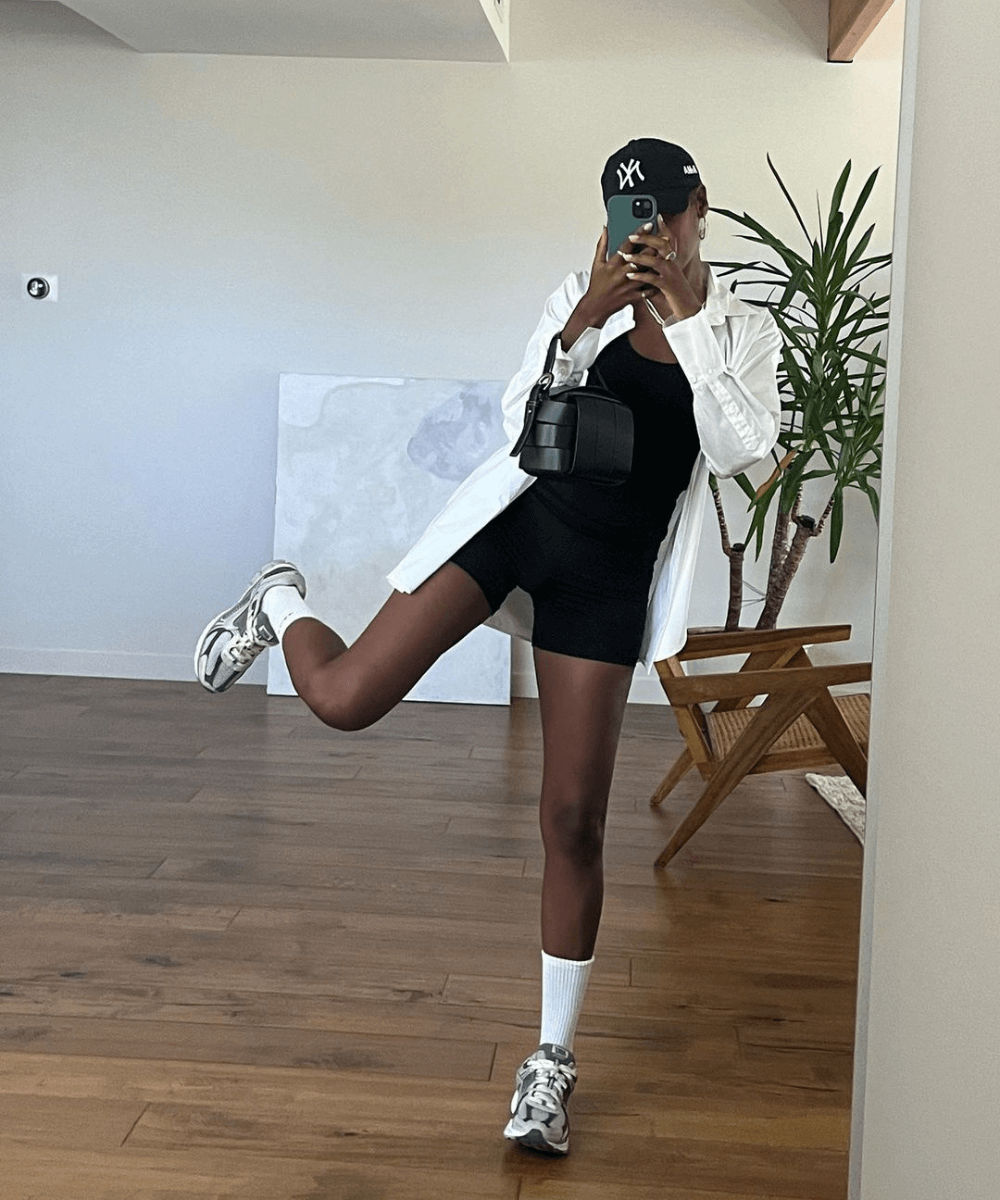 Claire Most - macaquinho fitness preto, camisa social branca, tênis com meias aparentes e boné - looks fáceis - verão - mulher negra tirando foto no espelho com uma das pernas levantadas - https://stealthelook.com.br