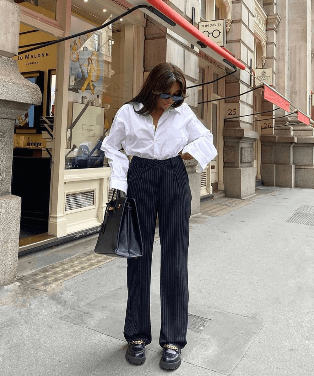 @bygigivassallo - calça preta risca de giz, mocassim preto e camisa branca oversized - look de trabalho - outono - mulher em pé na rua usando óculos de sol - https://stealthelook.com.br
