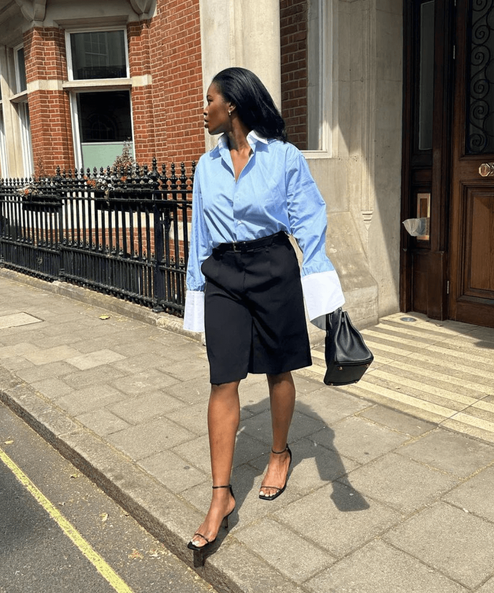 @lenafarl - bermuda de alfaiataria preta, camisa social azul e sandália de salto - look de trabalho - verão - mulher negra andando na rua segurando uma bolsa preta - https://stealthelook.com.br