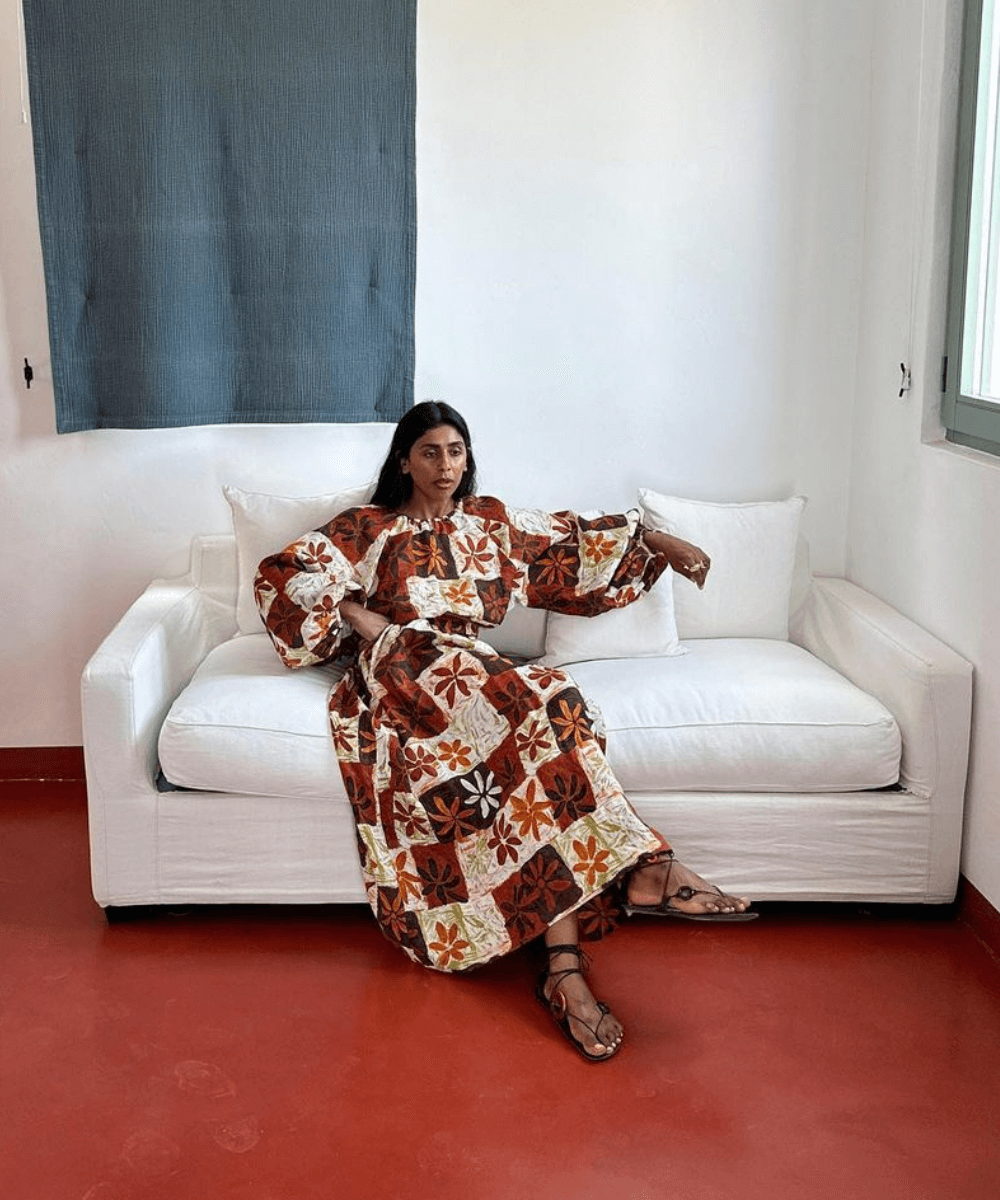 @monikh - vestido longo estampado em tons terrosos - verão 2024 - verão - mulher morena sentada em um sofá branco com as pernas cruzadas e braços esticados - https://stealthelook.com.br