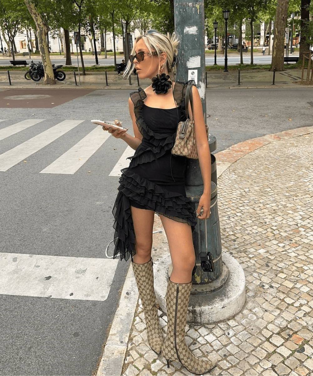 Sofia Coelho - vestido preto de babados curto e bota de cano longo estampada - tendência Y2K - verão - mulher loira em pé na rua usando óculos de sol - https://stealthelook.com.br