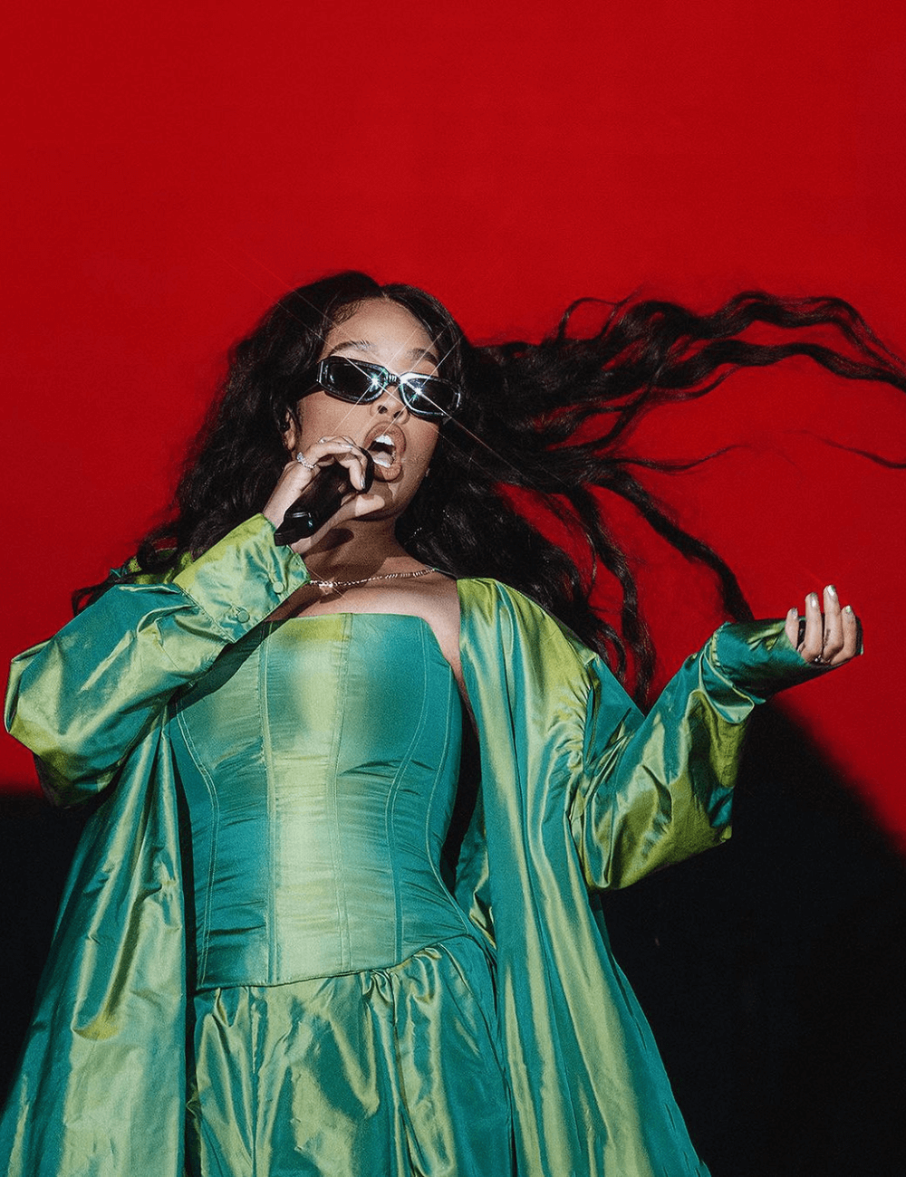 H.E.R - cojunto verde metalizado e óculos de sol - The Town - inverno - mulher negra cantando em um palco - https://stealthelook.com.br