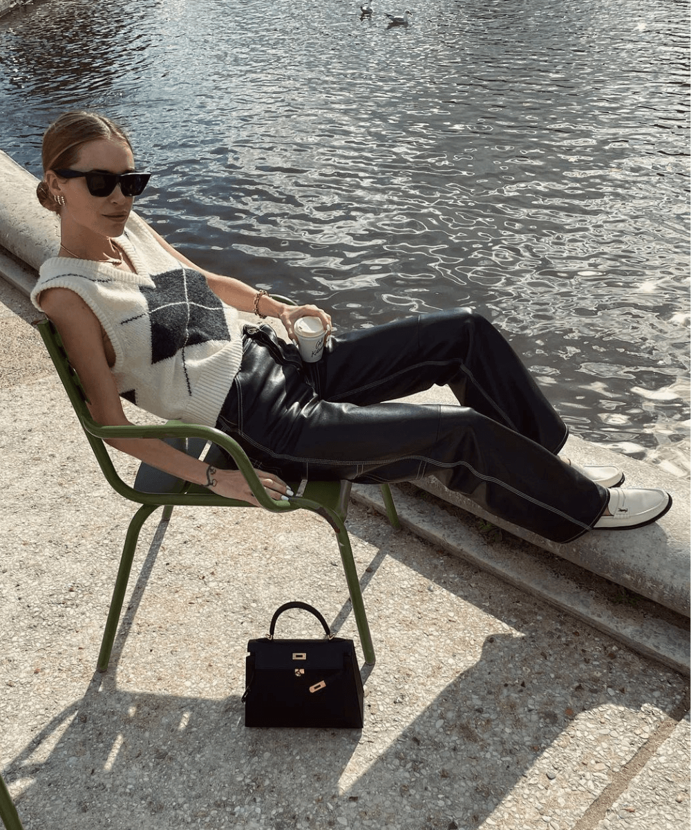 Pernille Teisbaek - colete de tricô bege com desenho preto, calça preta e tênis - Pernille Teisbaek - outono - mulher sentada em um banco na rua - https://stealthelook.com.br