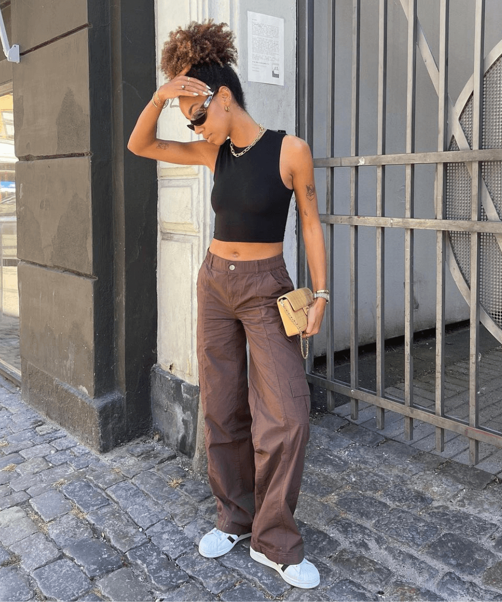 Amaka Hamelijnck - calça bag marrom, top preto e tênis adidas - tênis branco - outono - mulher negra em pé na rua com a mão no cabelo - https://stealthelook.com.br