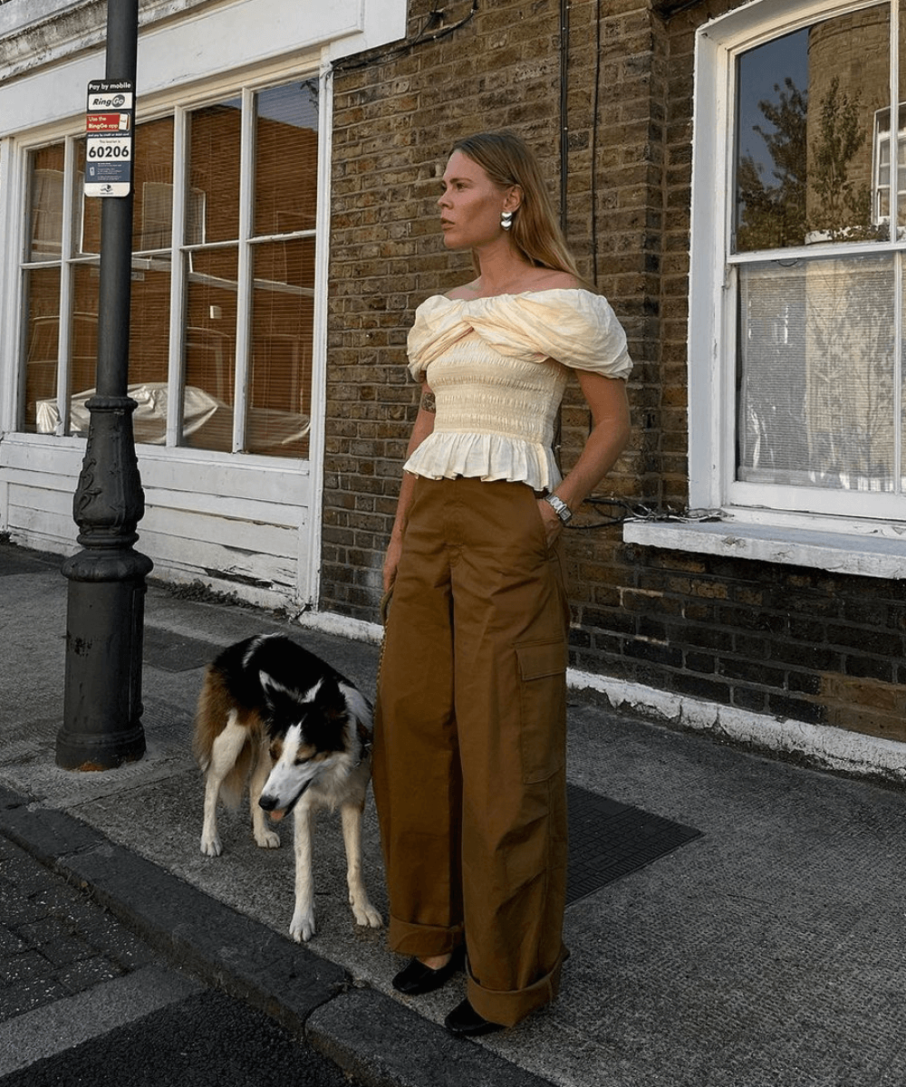 Jessie Bush - calça cargo marrom, blusa drapeada ombro a ombro - anos 2000 - verão - mulher loira em pé na rua ao lado de um cachorro - https://stealthelook.com.br