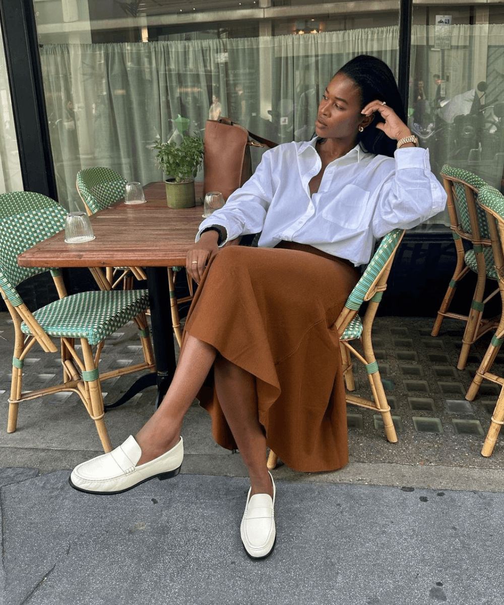 @nlmarilyn - saia midi marrom, blusa branca e mocassim off white - blusa branca - verão - mulher negra sentada em um café na rua com as pernas cruzadas - https://stealthelook.com.br