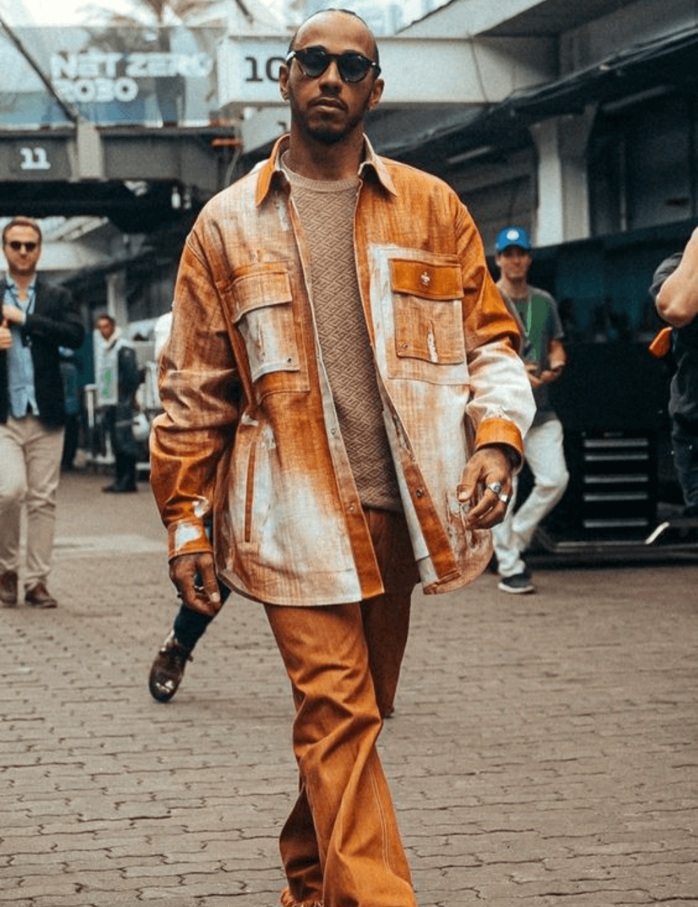 Lewis Hamilton - calça laranja, jaqueta laranja estampada, blusa branca e óculos de sol - Lewis Hamilton - outono - homem negro andando na rua usando óculos de sol - https://stealthelook.com.br