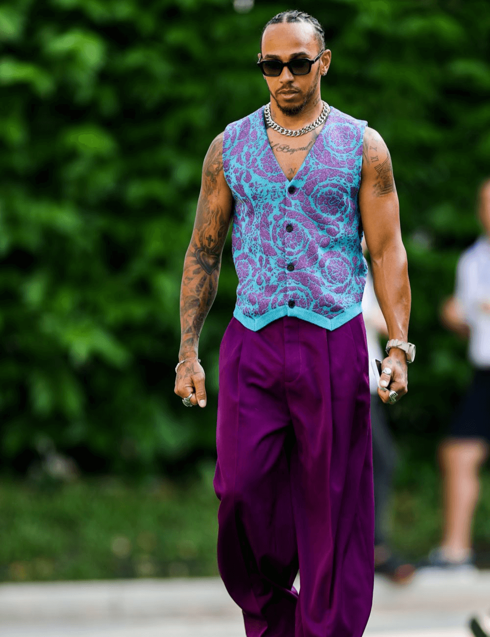 Lewis Hamilton - calça roxa e colete estampado roxo com azul - Lewis Hamilton - verão - homem negro andando na rua usando óculos de sol - https://stealthelook.com.br